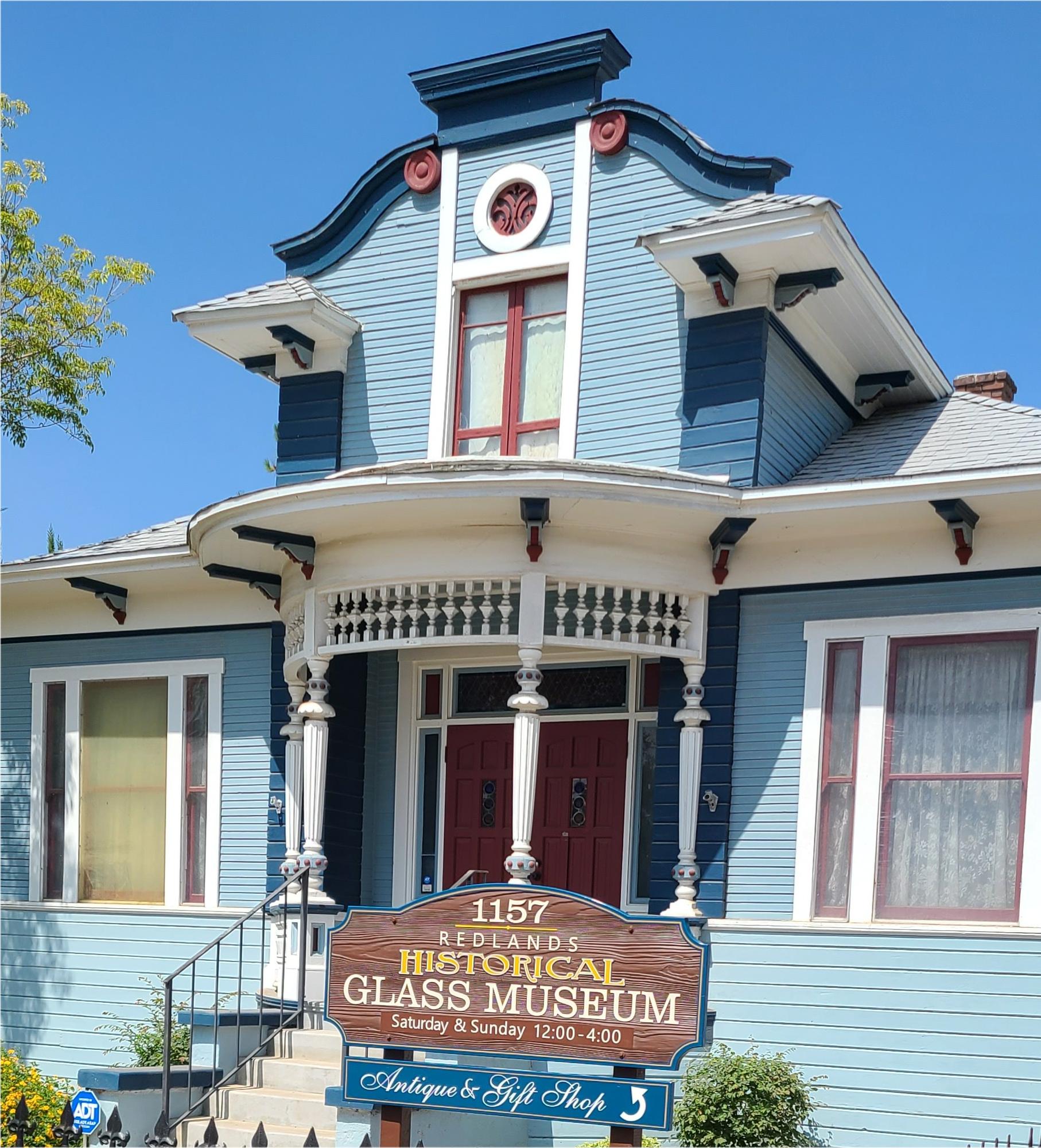 The blue Victorian Historical Glass Museum building and front museum sign in Redlands, California